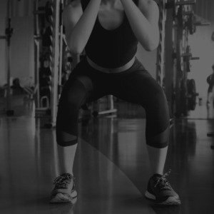 A woman squats in the gym with her hands on her knees.
