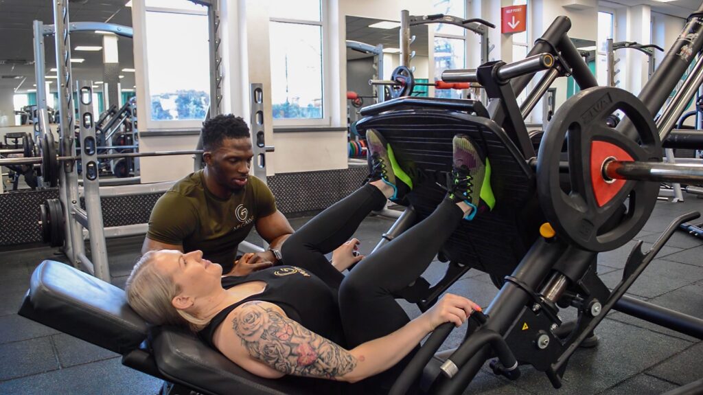 A man is working with another person on the gym equipment.